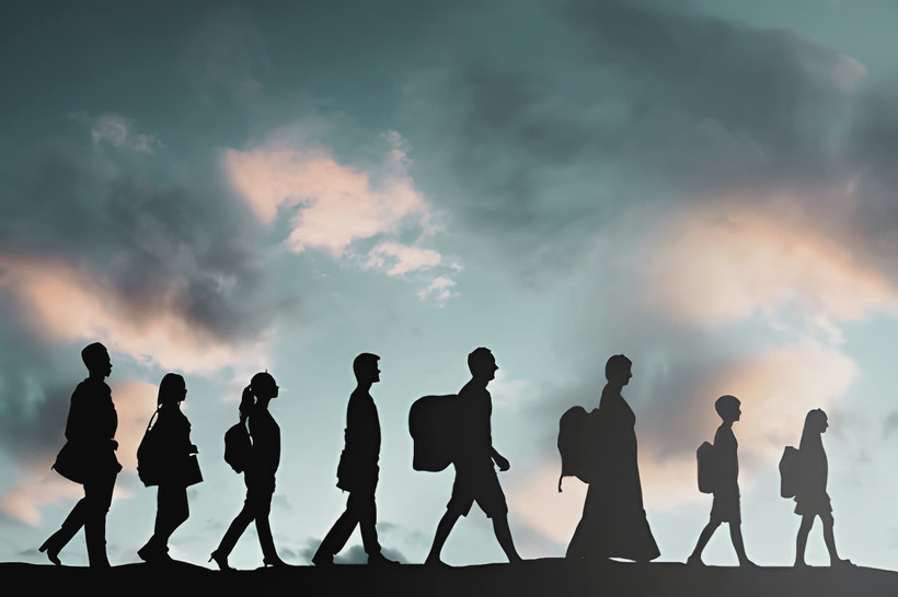 Silhouettes of people walking in a line against a cloudy sky